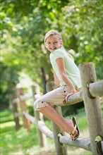 Portrait of girl (10-11) sitting on fence.