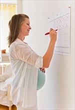 Young pregnant woman marking calendar.