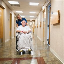 Young nurse is pushing senior man in wheelchair.