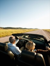 USA, Utah, Kanosh, Mad-adult couple driving through desert plains in convertible car. Photo: Erik