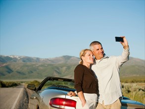 Mid adult couple photographing themselves in front of majestic mountain range.