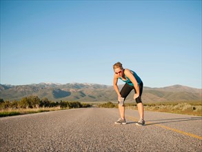 USA, Utah, Kanosh, Mid adult woman taking break from running on empty road.