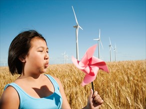 USA, Oregon, Wasco, Girl (10-11) holding blowing at fan in wheat field with wind turbines in