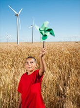 USA, Oregon, Wasco, Girl (10-11) holding fan in wheat field with wind turbines in background.
