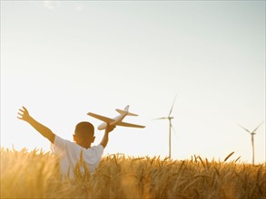 Boy (10-11) playing with toy aeroplane in wheat field.