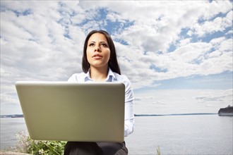Young businesswoman using laptop on lakeshore. Photo : Take A Pix Media