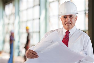 Portrait of senior man wearing tie and hardhat, holding blueprint. Photo : db2stock