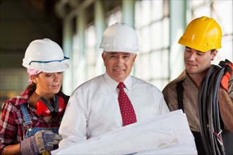 Portrait of manual workers and manager looking at blueprint. Photo: db2stock