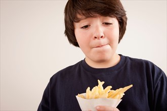 Studio portrait of boy (10-11) holding french fries. Photo : Rob Lewine