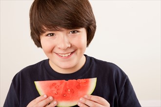 Studio portrait of boy (10-11) eating watermelon. Photo : Rob Lewine