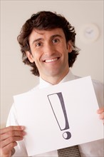 Studio portrait of businessman holding sheet of paper with exclamation mark. Photo : Rob Lewine