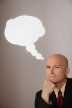 Studio shot of pensive business man with speech bubble above head. Photo : Rob Lewine