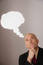 Studio shot of pensive business man with speech bubble above head. Photo : Rob Lewine