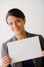 Smiling businesswoman holing blank page, studio shot. Photo: Rob Lewine