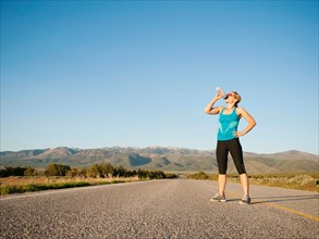 Mid adult woman drinking water while taking break from running on empty road. Photo: Erik Isakson