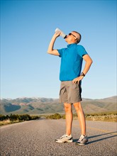 Mid adult an drinking water while taking break from running on empty road. Photo: Erik Isakson