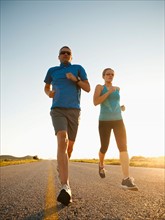 Mid adult couple running on empty road. Photo: Erik Isakson