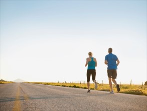 Mid adult couple running on empty road. Photo: Erik Isakson