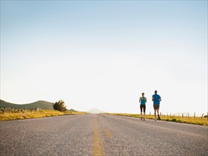 Mid adult couple running on empty road.