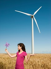 USA, Oregon, Wasco, Girl (12-13) holding fan in wheat field in front of wind turbines.