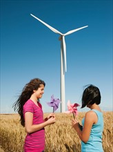 USA, Oregon, Wasco, Girl (10-11, 12-13) holding fans in wheat field in front of wind turbines.