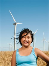 USA, Oregon, Wasco, Cheerful girl (10-11) standing in wheat field with wind turbines in background.