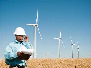 USA, Oregon, Wasco, Engineer standing in wheat field in front of wind turbines. Photo: Erik Isakson