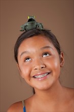 Studio portrait of girl (10-11) balancing plastic frog on head. Photo : Rob Lewine