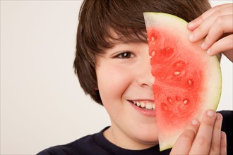 Studio portrait of boy (10-11) holding slice of watermelon. Photo : Rob Lewine