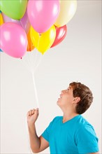Studio shot of boy (12-13) holding bunch of balloons. Photo : Rob Lewine