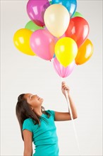 Portrait of smiling girl (10-11) holding balloons, studio shot. Photo : Rob Lewine