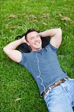 Man lying on grass listening to mp3 player. Photo : Take A Pix Media