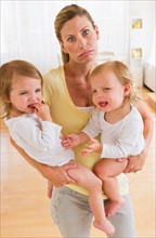 Mother holding crying daughters (2-3) and making facial expression.