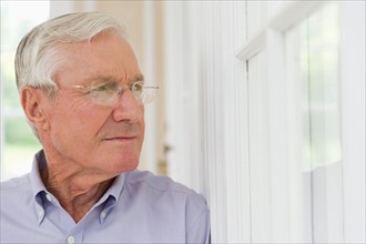 Portrait of senior man looking through window.