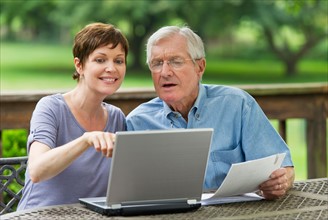 Senior father and adult daughter using laptop on porch.