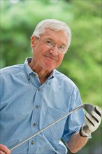 Senior man holding golf club, portrait.