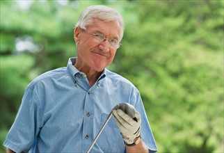 Senior man holding golf club, portrait.