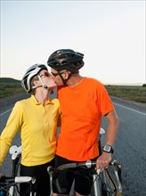 Couple of cyclists kissing on empty road.