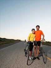Couple of cyclists posing for portrait on empty road.