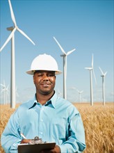 USA, Oregon, Wasco, Engineer standing in wheat field in front of wind turbines.