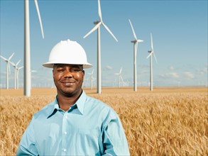 USA, Oregon, Wasco, Engineer standing in wheat field in front of wind turbines. Photo: Erik Isakson