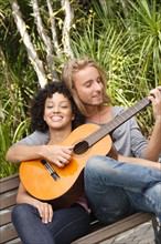 Young couple in park, man playing guitar. Photo : Rob Lewine