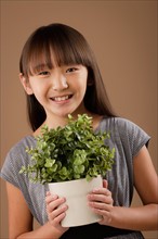 Studio portrait of girl (10-11) holding potted plant. Photo: Rob Lewine