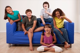 Group of children (10-11, 12-13) sitting on sofa, studio shot. Photo : Rob Lewine