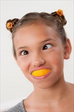 Studio portrait of girl (8-9) with slice of lemon in mouth. Photo : Rob Lewine