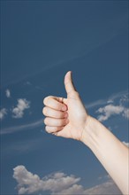 Woman's hand showing thumbs-up gesture against sky. Photo: Winslow Productions