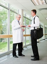 Doctor talking talking with pharmaceutical representative in hospital corridor.