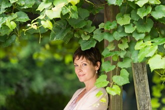 Portrait of mature woman leaning against wooden post overgrown with ivy.