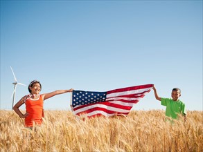 USA, Oregon, Wasco, Girl (10-110 and boy (8-9) holding american flag in wheat field, wind turbine