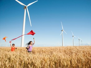 USA, Oregon, Wasco, Girls (10-11, 12-13) playing with kite in wheat field, wind turbines in